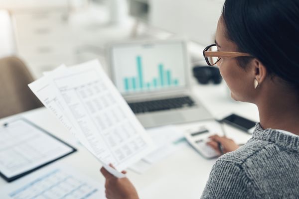 Woman-with-paper-graphs-iStock-1330234595-400x600-1 Woman reviewing data while sitting at at desk